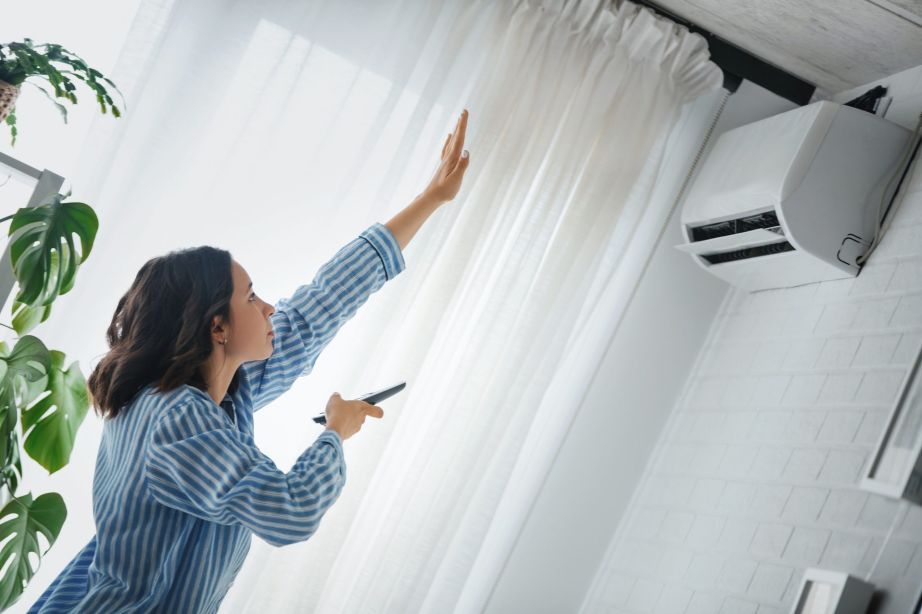 A woman turning on an AC unit with remote control and checking the temperature